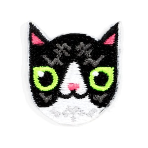 May include: Black and white cat face embroidered patch with green eyes and pink nose.
