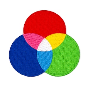 May include: A colorful embroidered patch featuring three overlapping circles in red, blue, green, yellow, pink, and white. The circles are arranged in a triangular shape.