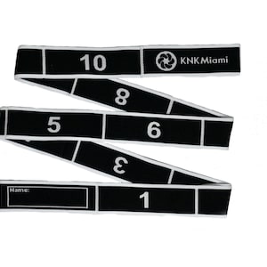 May include: Black and white fabric measuring tape with numbers 1 through 10, a logo that says "KNK Miami", and a blank space for a name.