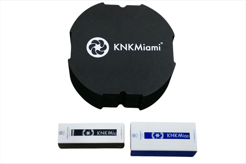 May include: A black round container with the text "KNKMiami" and a white logo. Two rectangular boxes with the text "KNKMiami" and a white logo. The boxes are white with blue accents.