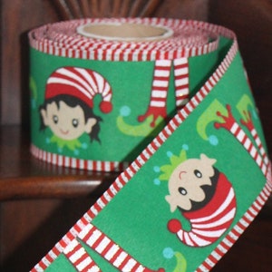 May include: Green Christmas ribbon featuring elf faces, striped legs, and red and white striped trim. The ribbon is rolled and unrolled, showcasing the repeating pattern. Perfect for holiday crafts and gift wrapping.
