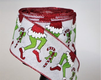 May include: White ribbon with a red trim and a repeating pattern of green Grinch legs wearing red boots and a Santa hat with a candy cane.