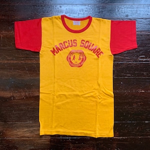 May include: A vintage yellow and red raglan t-shirt. The shirt features the text "MARCUS SQUARE" in red block letters above a red emblem. The shirt has a crew neck and short sleeves.