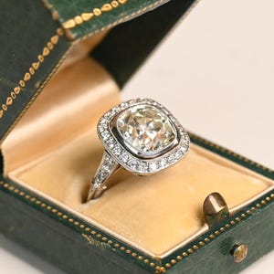 Anillo de compromiso con diamante talla cojín antiguo de 4 quilates. Engaste biselado. Anillo con halo de diamantes talla europea antigua. Fabricado en platino.