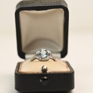 0,70 ct rundslipad akvamarinring i blommig stil med halo-diamantaccent. Ring med födelsesten i mars. Ring i platina. Födelsesten i akvamarin.