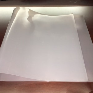 May include: A white, flexible sheet of plastic, folded in half, on a wooden surface.