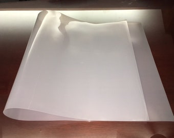 May include: A white, flexible sheet of plastic, folded in half, on a wooden surface.