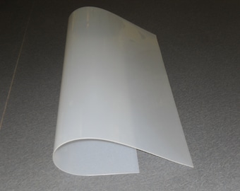 May include: A white, flexible sheet of plastic, rolled up and lying on a gray surface.