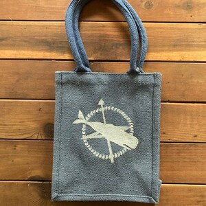 May include: A blue tote bag made of burlap with a white whale and compass design. The bag has two blue handles.