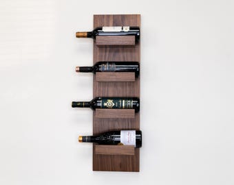 May include: A wall-mounted wine rack made of dark wood with four shelves. Each shelf has a metal lip to hold wine bottles. The rack is holding four bottles of wine.
