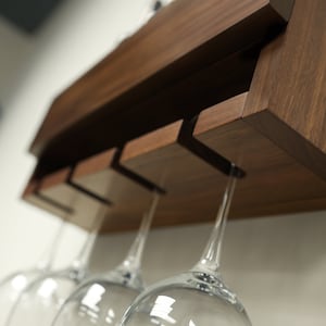 May include: A wooden wall-mounted wine glass rack with four glass holders. The rack is made of dark brown wood and has a simple, modern design.