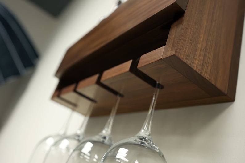 May include: A wooden wall-mounted wine glass rack with four glass holders. The rack is made of dark brown wood and has a simple, modern design.