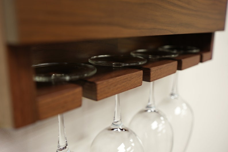 May include: A wooden wine glass rack with four wine glasses hanging from it. The rack is mounted on a wall and has a dark wood finish.