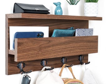 May include: A dark brown wooden wall organiser with a shelf, a mail slot, and four hooks. The organiser holds a black wallet, a blue phone, and other items. A blue ceramic bird and plants are on the shelf. The hooks hold bags and keys.