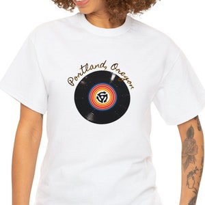 May include: White t-shirt featuring a black vinyl record graphic and the text "Portland, Oregon" in gold script.
