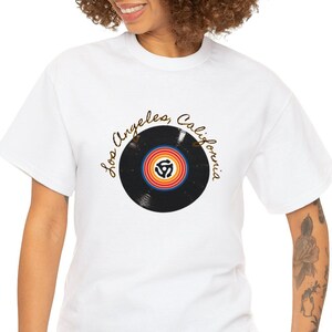 May include: White t-shirt featuring a black vinyl record graphic and the text "Los Angeles, California" in gold script.