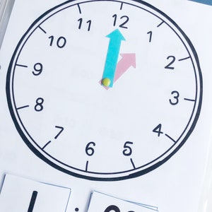 May include: A black and white clock face with the numbers 1 through 12. The hour hand is pointing at the 12 and the minute hand is pointing at the 12. The time is 1:00.