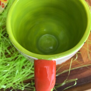 May include: A green ceramic mug with an orange handle. The mug is empty and has a glossy finish.