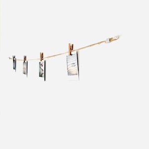 May include: A string of photos hanging on a white wall with wooden clothespins. The photos are in black and white and color.