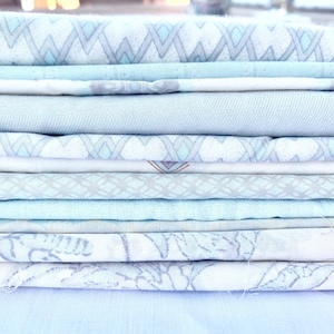 May include: A stack of light blue fabric scraps with various patterns, including geometric, floral, and abstract designs.