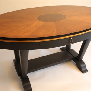 May include: An oval wooden table with a black base and a gold trim. The table top has a sunburst design with a dark wood centre.