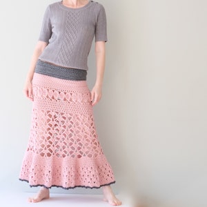 May include: A light pink crochet skirt with a gray trim and a gray waistband. The skirt has an open, lacy design and a flared bottom. The model is also wearing a gray short-sleeved shirt.