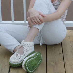Op de afbeelding: Handgemaakte gehaakte pantoffels in cr&egrave;me en groen. De pantoffels hebben een gesloten ontwerp met een band over de bovenkant van de voet. De zolen zijn groen met een witte rand. De pantoffels zijn ontworpen voor binnenshuis.
