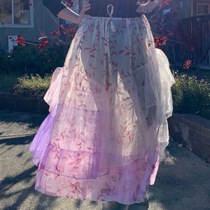 May include: A layered skirt with a floral pattern in shades of pink and purple. The skirt has multiple tiers of sheer fabric, creating a flowing and ethereal look. The top is a dark color.