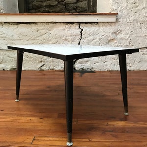 May include: A white marble top coffee table with black legs and gold accents. The table has a simple, mid-century modern design.