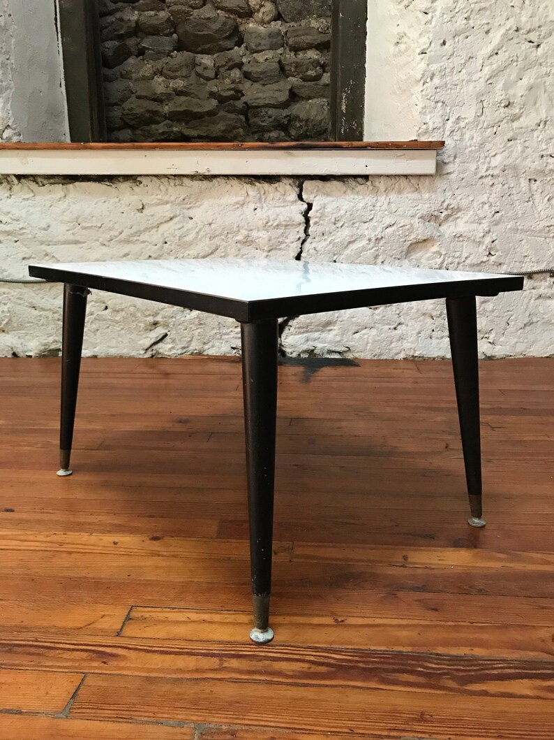 May include: A white marble top coffee table with black legs and gold accents. The table has a simple, mid-century modern design.