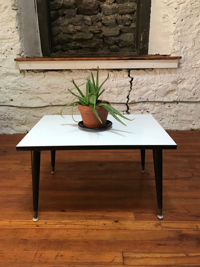 May include: A white coffee table with black legs and a black trim around the edge of the tabletop. A potted plant sits on the table.