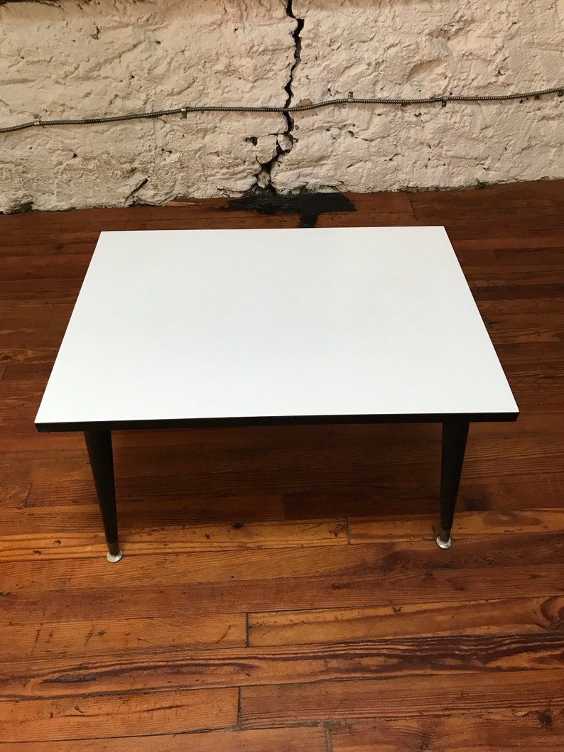 May include: A white square coffee table with black legs. The table is sitting on a wooden floor.
