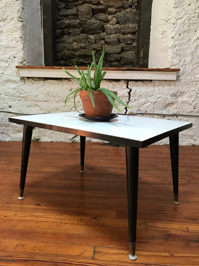 May include: A white mid-century modern coffee table with black legs and a plant in a terracotta pot on top.