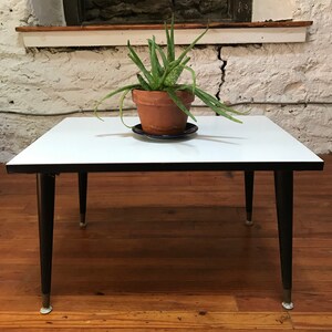 May include: A white mid-century modern coffee table with black legs and a plant in a terracotta pot on top.