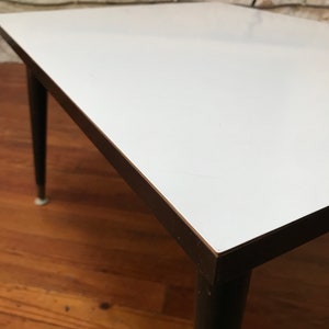 May include: A white square coffee table with a black wood frame and legs. The table is sitting on a wooden floor.