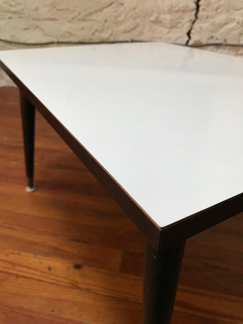 May include: A white square coffee table with a black wood frame and legs. The table is sitting on a wooden floor.