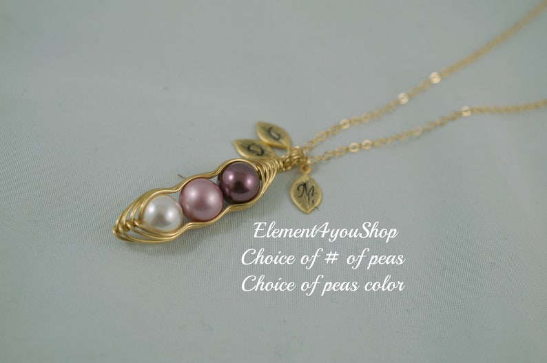 May include: A gold-colored necklace featuring a pea pod design with three pearl beads in white, pink, and purple. The necklace includes leaf charms and the text "Element4youShop".