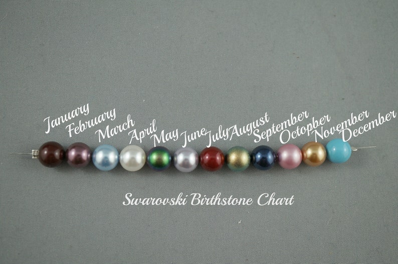 May include: A Swarovski birthstone chart featuring a row of twelve colorful beads, each representing a month of the year. The beads are in various colors, including brown, purple, blue, white, green, and red. The text "Swarovski Birthstone Chart" is below the beads.