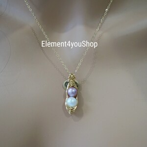 May include: A gold-colored necklace with a pendant shaped like a pea pod. The pea pod contains two pearls, one lavender and one white. The necklace chain is delicate. The text "Element4youShop" is visible.