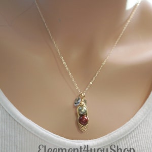 May include: A gold-colored necklace with a pendant featuring two round beads, one green and one red, encased in a wire design. The necklace also has small, clear accent beads. The text "Eleement4youShop" is visible.