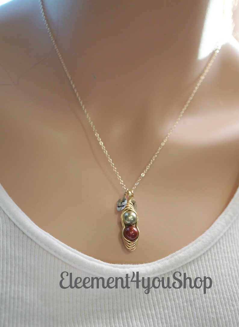 May include: A gold-colored necklace with a pendant featuring two round beads, one green and one red, encased in a wire design. The necklace also has small, clear accent beads. The text "Eleement4youShop" is visible.