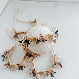 Puede incluir: Un conjunto de diademas florales y una esfera decorativa. Las diademas presentan flores secas en tonos rosa, blanco y verde, acentuadas con cintas beige. La esfera est&aacute; envuelta en tela blanca, creando una est&eacute;tica suave y natural. Ideal para fotograf&iacute;a de reci&eacute;n nacidos.