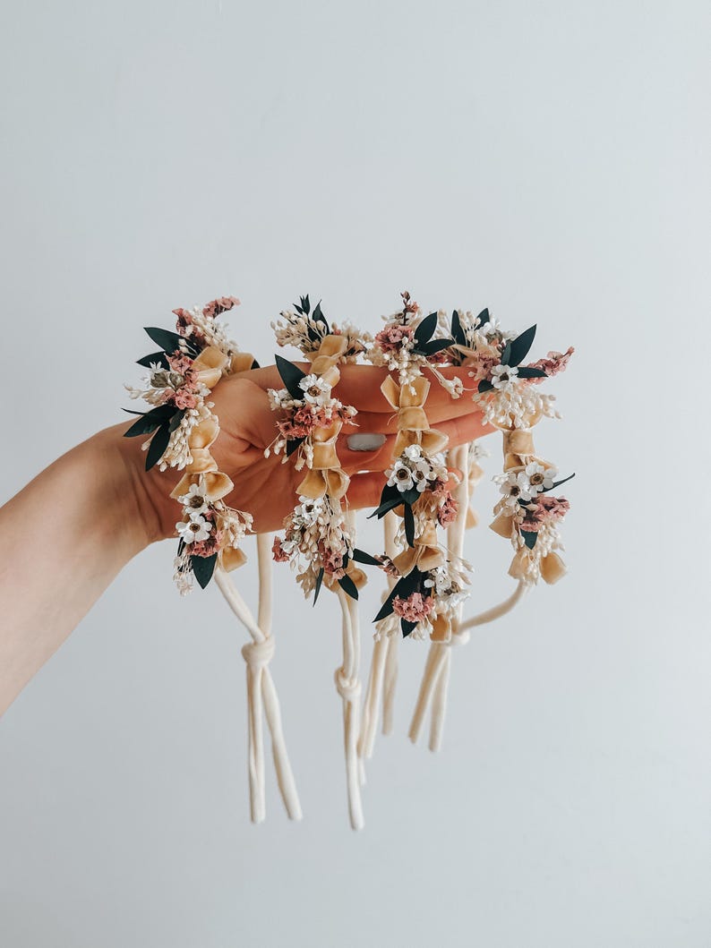 Puede incluir: Una colecci&oacute;n de accesorios florales para el cabello. Cada pieza presenta una base de color crema adornada con peque&ntilde;as flores rosas, blancas y verdes. Los accesorios se mantienen unidos con cordones de color crema, creando una est&eacute;tica delicada y natural.