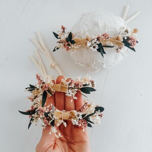 Puede incluir: Dos diademas florales con base de cinta de terciopelo beige. Las diademas est&aacute;n adornadas con peque&ntilde;as flores rosas, blancas y verdes. Una diadema est&aacute; sobre un objeto esf&eacute;rico blanco, y la otra se sostiene en una mano.