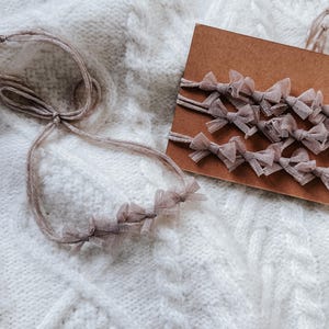 May include: A set of five brown tulle bows with a brown string attached to each bow. The bows are arranged on a brown card.