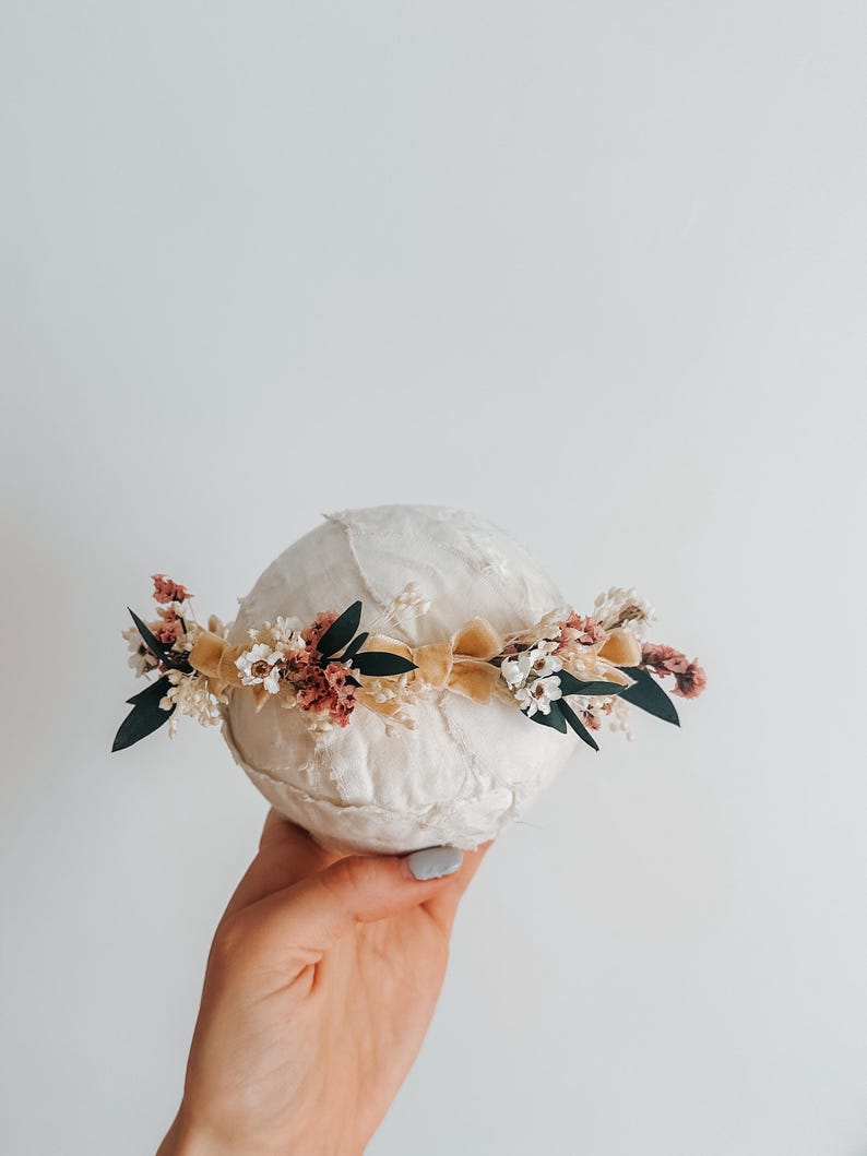 Puede incluir: Una corona floral crema con flores secas en tonos rosa, blanco y verde, acentuada por una cinta amarilla suave. La corona est&aacute; dise&ntilde;ada para un beb&eacute; o ni&ntilde;o, perfecta para una sesi&oacute;n de fotos o una ocasi&oacute;n especial.
