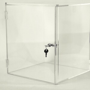 K&ouml;nnte beinhalten: Ein transparentes Acryl-Vitrinen-Display mit Schloss und Schl&uuml;ssel. Die Vitrine ist w&uuml;rfelf&ouml;rmig und hat eine Fl&uuml;gelt&uuml;r.