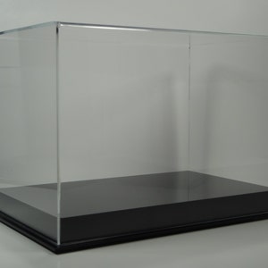 May include: A clear acrylic display case with a black base. The case has a rectangular shape and is designed to protect and showcase items.