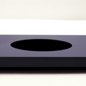 May include: A black, rectangular, modern tissue box cover with a circular opening in the center. The tissue box cover is made of a glossy material and sits on a flat base.