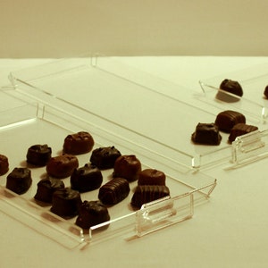 K&ouml;nnte beinhalten: Drei transparente Acryl-Tabletts mit Schokoladenbonbons auf dem oberen Tablett. Die Tabletts sind &uuml;bereinander gestapelt.